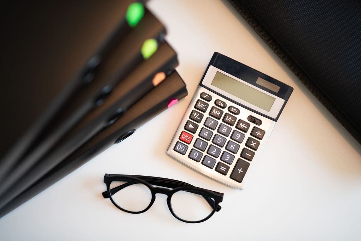 Calculatrice, lunettes et dossiers posés sur un bureau clair