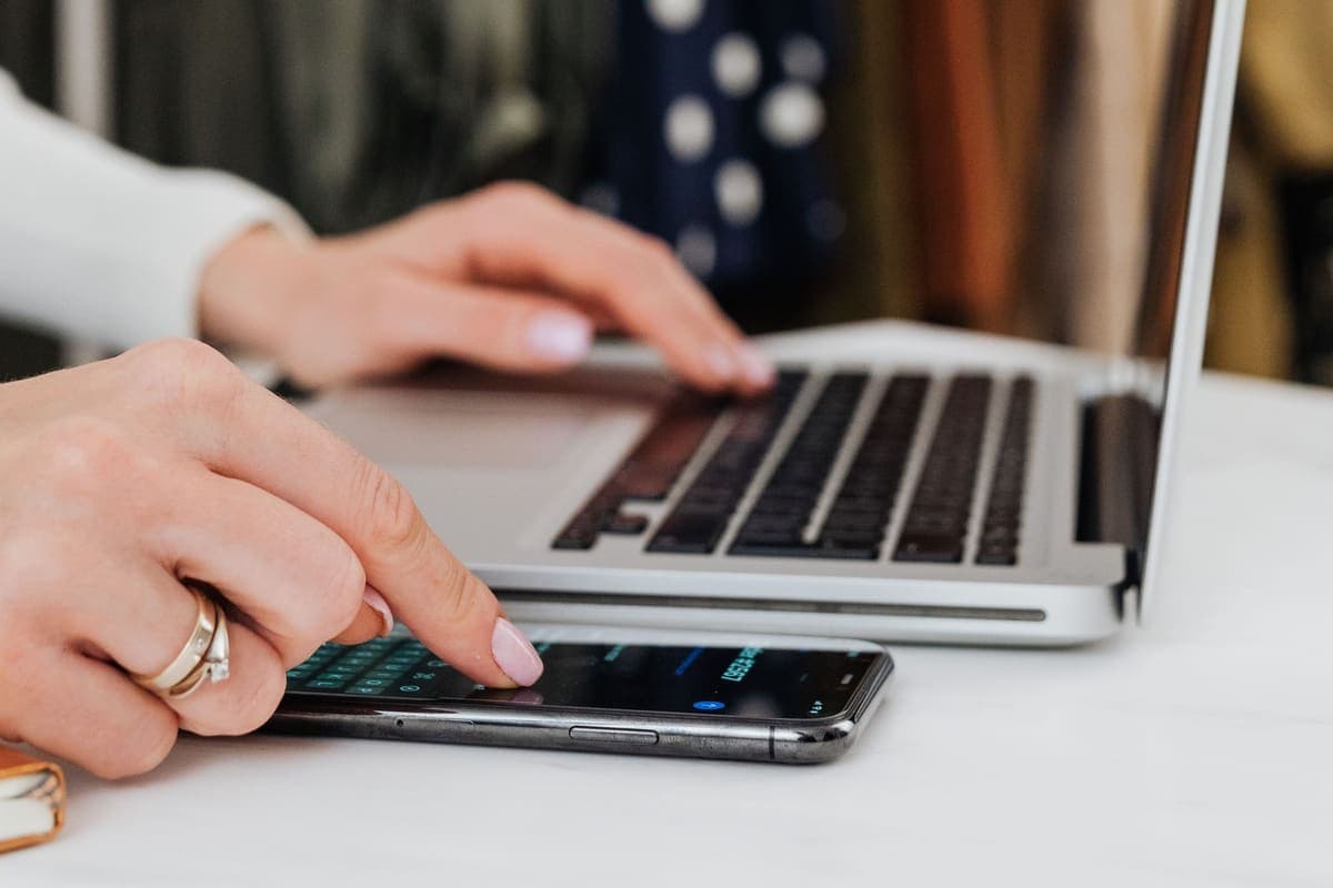 Mains rédigeant une annonce de vêtement sur un ordinateur portable, portant à vêtements en arrière-plan
