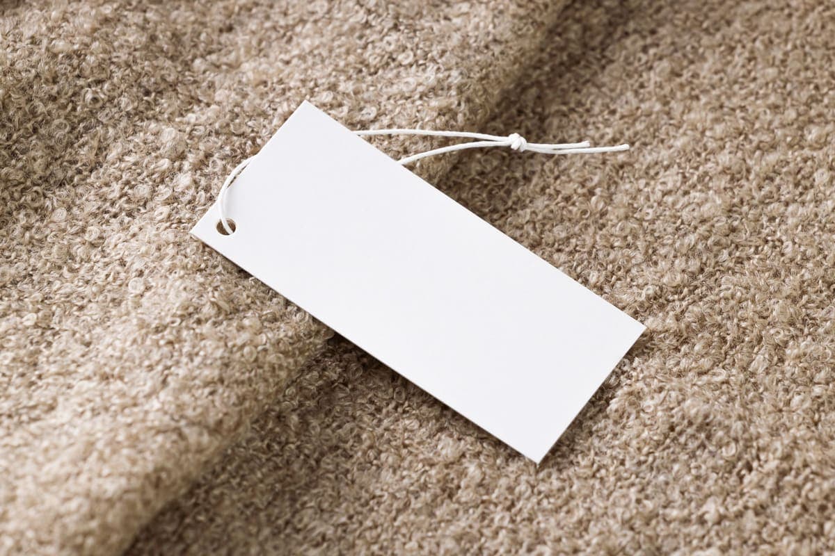 Étiquette de prix vierge posée sur un lainage beige, prête à être renseignée