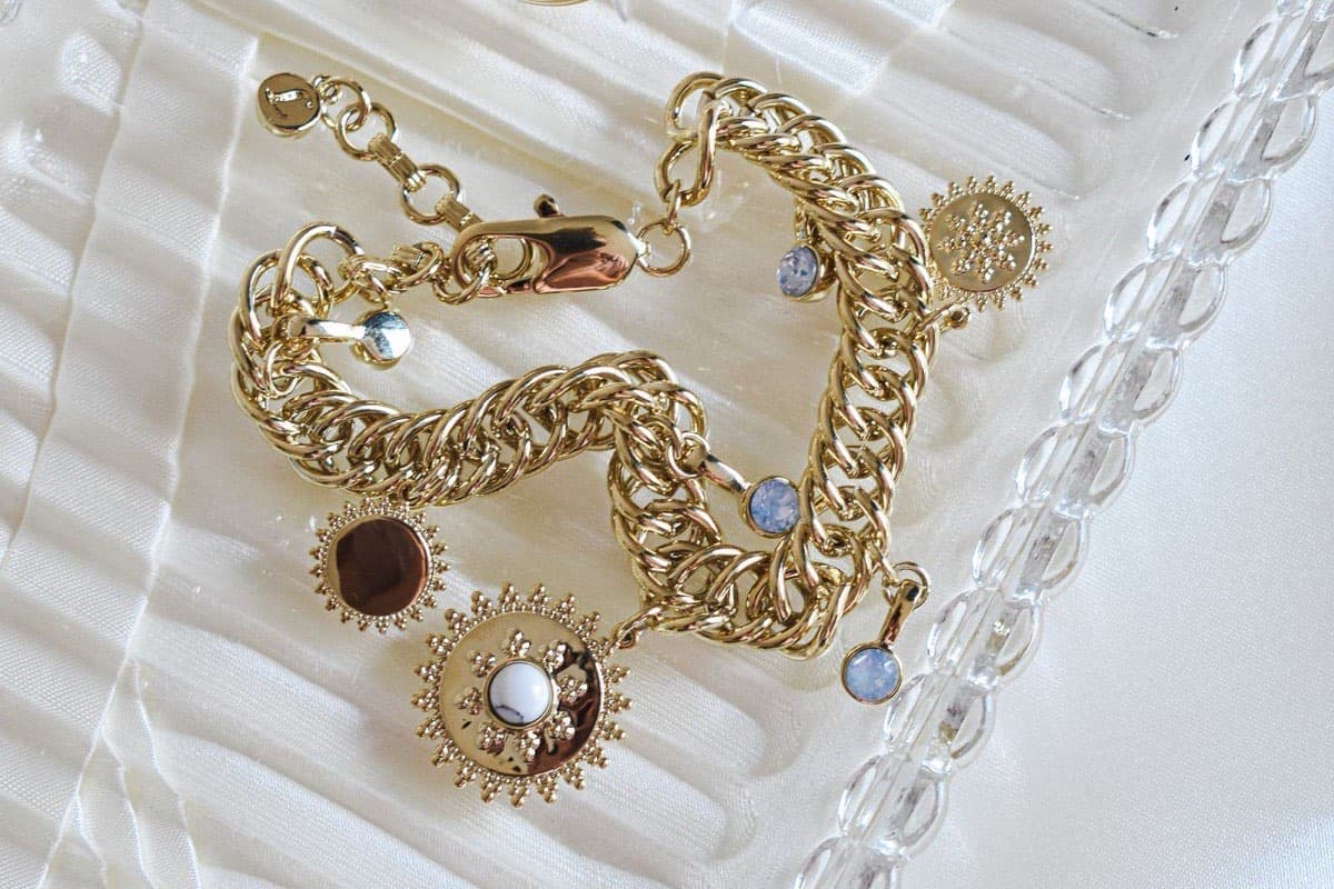 Bracelet en or à breloques photographié en gros plan sur un plateau de verre