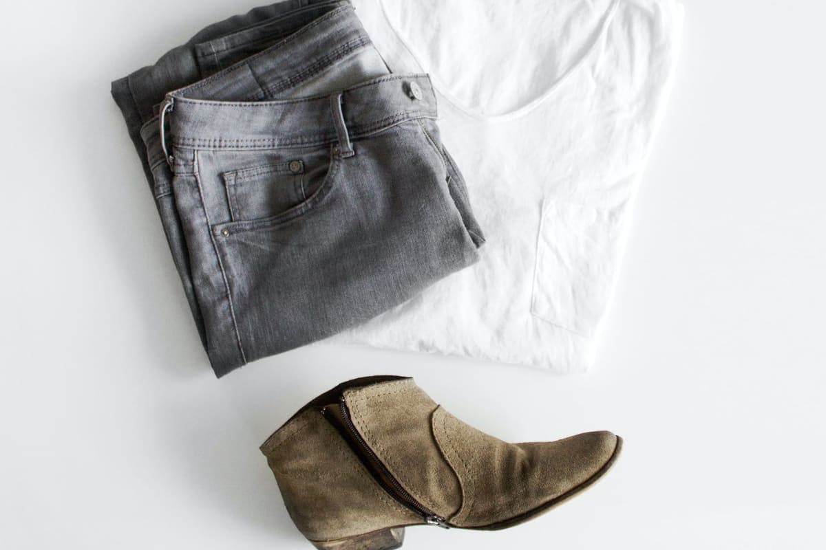 Jean gris plié, tee-shirt blanc et bottine en daim disposés à plat sur fond blanc